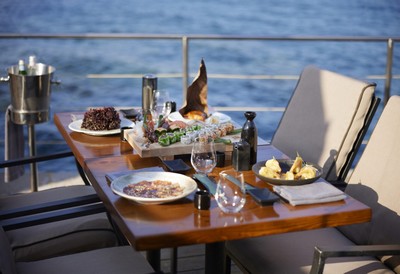 Elegant seaside dining setup at the Elounda Peninsula All Suite Hotel, featuring gourmet dishes on a wooden table with a breathtaking ocean view. Elegant seaside dining setup at the Elounda Peninsula All Suite Hotel, featuring gourmet dishes on a wooden table with a breathtaking ocean view.