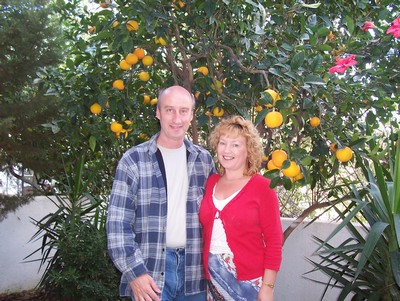 A happy, smiling couple posing in front of a lush orange tree in Crete, surrounded by greenery and bright citrus fruits. A happy, smiling couple posing in front of a lush orange tree in Crete, surrounded by greenery and bright citrus fruits.