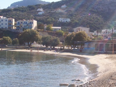 A tranquil view of Almyrida Beach in Crete, Greece, featuring calm waters, sandy shoreline, and charming hillside buildings nestled among lush greenery.