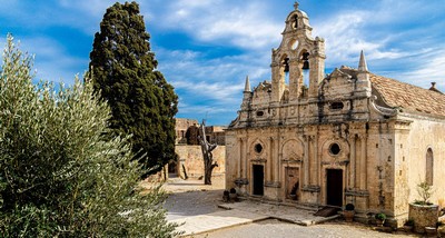 Historic Arkadi Monastery in Crete, Greece, featuring a beautiful Venetian-style facade, surrounded by lush greenery and a bright blue sky.