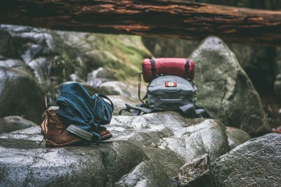 Essential hiking gear, including a backpack, boots, and rolled-up clothing, resting on rugged rocks in a scenic outdoor setting. Essential hiking gear, including a backpack, boots, and rolled-up clothing, resting on rugged rocks in a scenic outdoor setting.