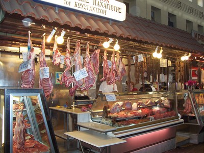 Butcher stall at Chania Market, Crete, displaying a variety of fresh meats hanging and arranged in cases, illuminated under warm lights. Butcher stall at Chania Market, Crete, displaying a variety of fresh meats hanging and arranged in cases, illuminated under warm lights.