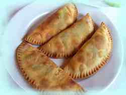 A plate of traditional Cretan cheese pies (kalitsounia), golden-brown and half-moon shaped, with crimped edges. A plate of traditional Cretan cheese pies (kalitsounia), golden-brown and half-moon shaped, with crimped edges.