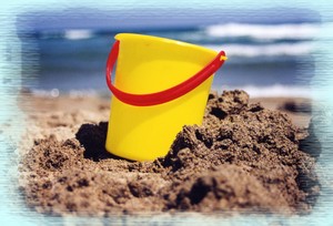 A kids yellow beach bucket on golden sands.