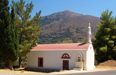 Cretan chapel surrounded by cypress trees at the foot of a mountain under a blue sky. Cretan chapel surrounded by cypress trees at the foot of a mountain under a blue sky.