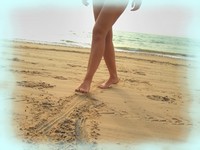 Close-up of a person walking barefoot along a sandy beach, with soft waves in the background and a serene coastal atmosphere. Close-up of a person walking barefoot along a sandy beach, with soft waves in the background and a serene coastal atmosphere.