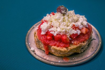 Image of traditional Cretan Dakos Salad: A savoury delight made with barley rusks, fresh tomato, crumbled feta cheese, olive oil, and a garnish of herbs and olives.