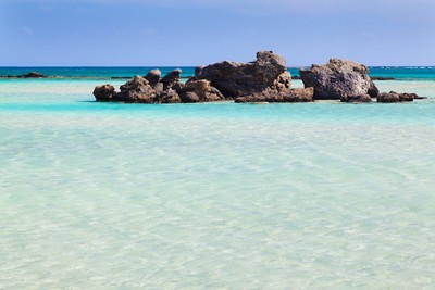 Clear turquoise waters surrounding rocks at Elafonissi Beach in Crete, Greece, with a pristine, shallow lagoon and vibrant shades of blue in the background. This popular beach is known for its stunning, exotic beauty and peaceful atmosphere. Clear turquoise waters surrounding rocks at Elafonissi Beach in Crete, Greece, with a pristine, shallow lagoon and vibrant shades of blue in the background. This popular beach is known for its stunning, exotic beauty and peaceful atmosphere.