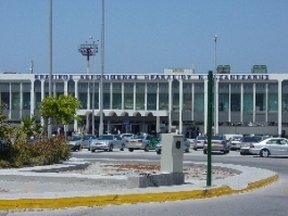 Heraklion Airport exterior view with a bustling entrance, cars parked in the foreground, and clear signage above the main building. Heraklion Airport exterior view with a bustling entrance, cars parked in the foreground, and clear signage above the main building.