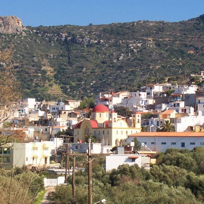 Kalyves, a picturesque Cretan village nestled at the foot of rocky hills, featuring whitewashed houses and a church with a striking red dome.