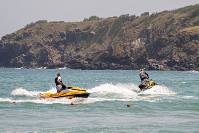 Two people riding jet skis on a sunny day in Crete, Greece, with waves splashing around them and a rocky hillside in the background. The scene captures the excitement of water sports in the beautiful Mediterranean waters. Two people riding jet skis on a sunny day in Crete, Greece, with waves splashing around them and a rocky hillside in the background. The scene captures the excitement of water sports in the beautiful Mediterranean waters.