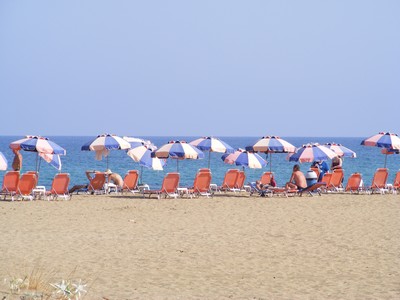 A sandy beach in Malia, Crete, lined with sunbeds and colourful umbrellas. Tourists relax by the shore, enjoying the clear blue waters of the Mediterranean under a bright summer sky. A sandy beach in Malia, Crete, lined with sunbeds and colourful umbrellas. Tourists relax by the shore, enjoying the clear blue waters of the Mediterranean under a bright summer sky.