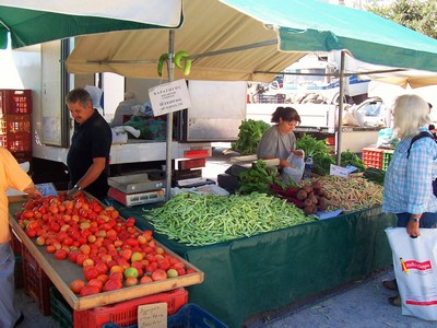 Local vendors at a bustling market stall in Agios Nikolaos, Crete, offering vibrant tomatoes, fresh green beans, and other seasonal produce to eager shoppers. Local vendors at a bustling market stall in Agios Nikolaos, Crete, offering vibrant tomatoes, fresh green beans, and other seasonal produce to eager shoppers.