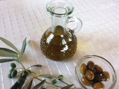 A glass carafe of golden olive oil alongside a bowl of olives and fresh olive branches, representing Crete's rich olive heritage. A glass carafe of golden olive oil alongside a bowl of olives and fresh olive branches, representing Crete's rich olive heritage.