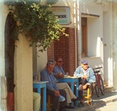 Elderly Cretan men sitting at a traditional kafeneion, enjoying Raki and conversation at blue wooden tables outside a whitewashed village café. Elderly Cretan men sitting at a traditional kafeneion, enjoying Raki and conversation at blue wooden tables outside a whitewashed village café.