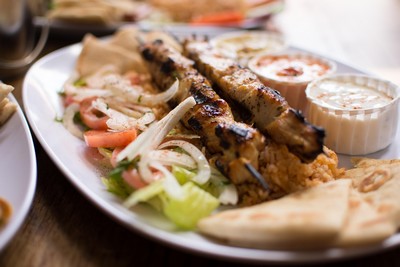 A plate of Greek souvlaki featuring two skewers of grilled, marinated meat served with fresh salad, fluffy rice, warm pita bread, and creamy tzatziki sauce. The dish is beautifully presented with vibrant colors and rich textures, capturing the essence of Mediterranean cuisine.
