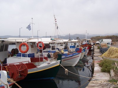 Colorful fishing boats docked along a quiet pier in Kissamos, with fishing nets and supplies scattered nearby, capturing the traditional coastal life in Crete.